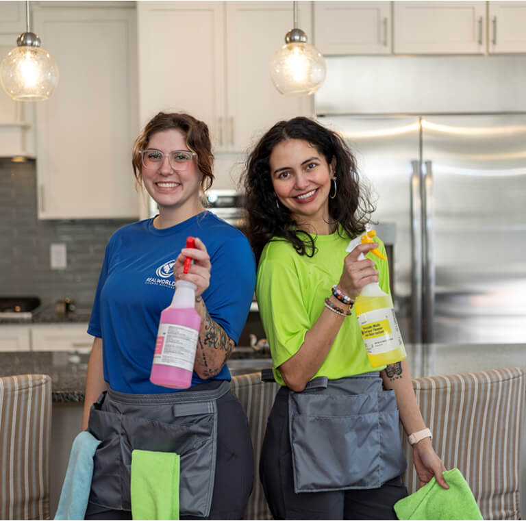 Two cleaning technicians standing back to back holding spray bottles